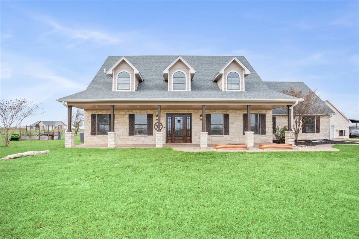Cape cod-style house featuring a porch, a front lawn, roof with shingles, and stone siding