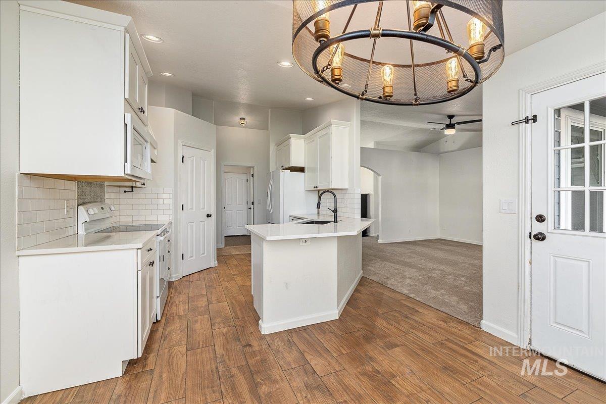 411 Hawthorne Street Nampa, ID 83686 - Photo 6 of 48 Kitchen with white cabinets, decorative backsplash, white appliances, a chandelier, and arched walkways