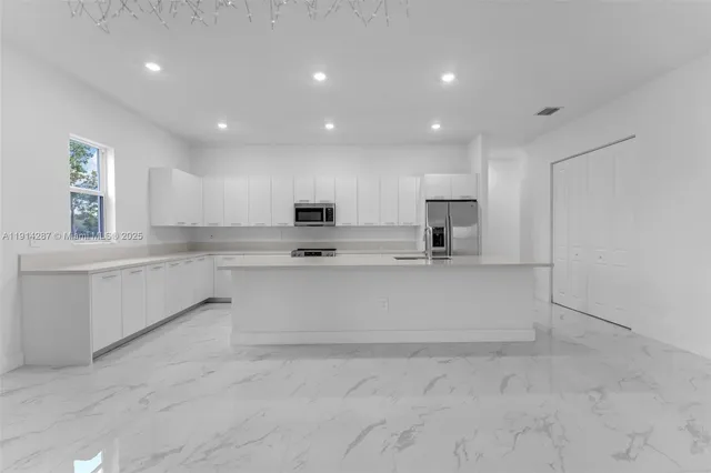 a large white kitchen with kitchen island a sink stainless steel appliances and a cabinets