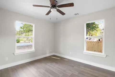 an empty room with wooden floor fan and windows
