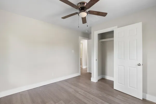 an empty room with wooden floor fan and windows