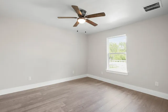 an empty room with wooden floor ceiling fan and windows