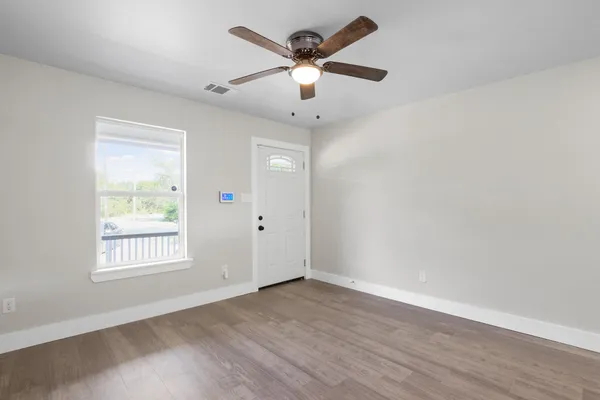 an empty room with wooden floor ceiling fan and windows