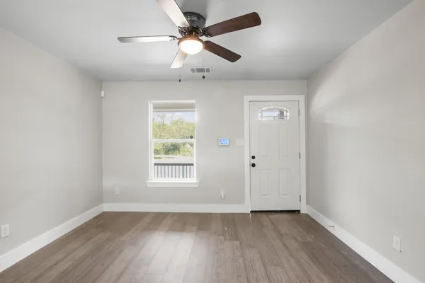 an empty room with wooden floor ceiling fan and windows