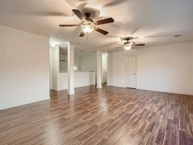 a view of an empty room with wooden floor and a ceiling fan