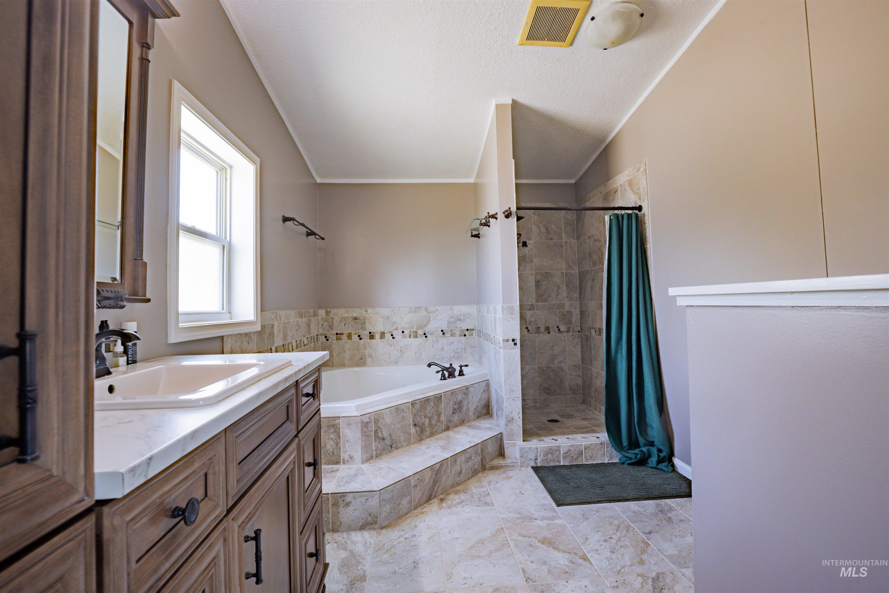 23904 Southview Lane Middleton, ID 83644 - Photo 28 of 29 Bathroom featuring a wood-finish vanity with a built-in sink, a built-in tub with tile surround, a tiled shower enclosure, and a window