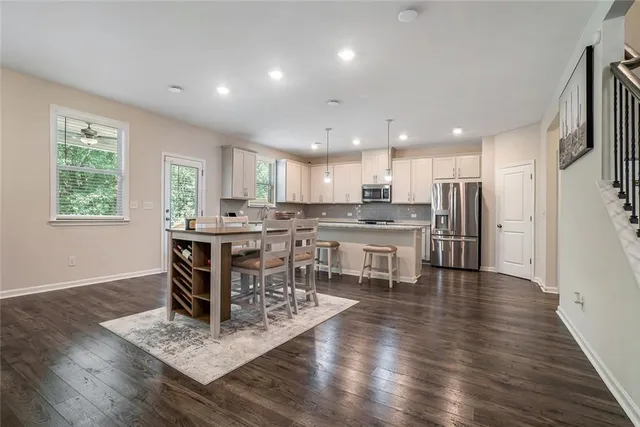 a kitchen with stainless steel appliances kitchen island granite countertop a stove a refrigerator a sink a dining table and chairs with wooden floor