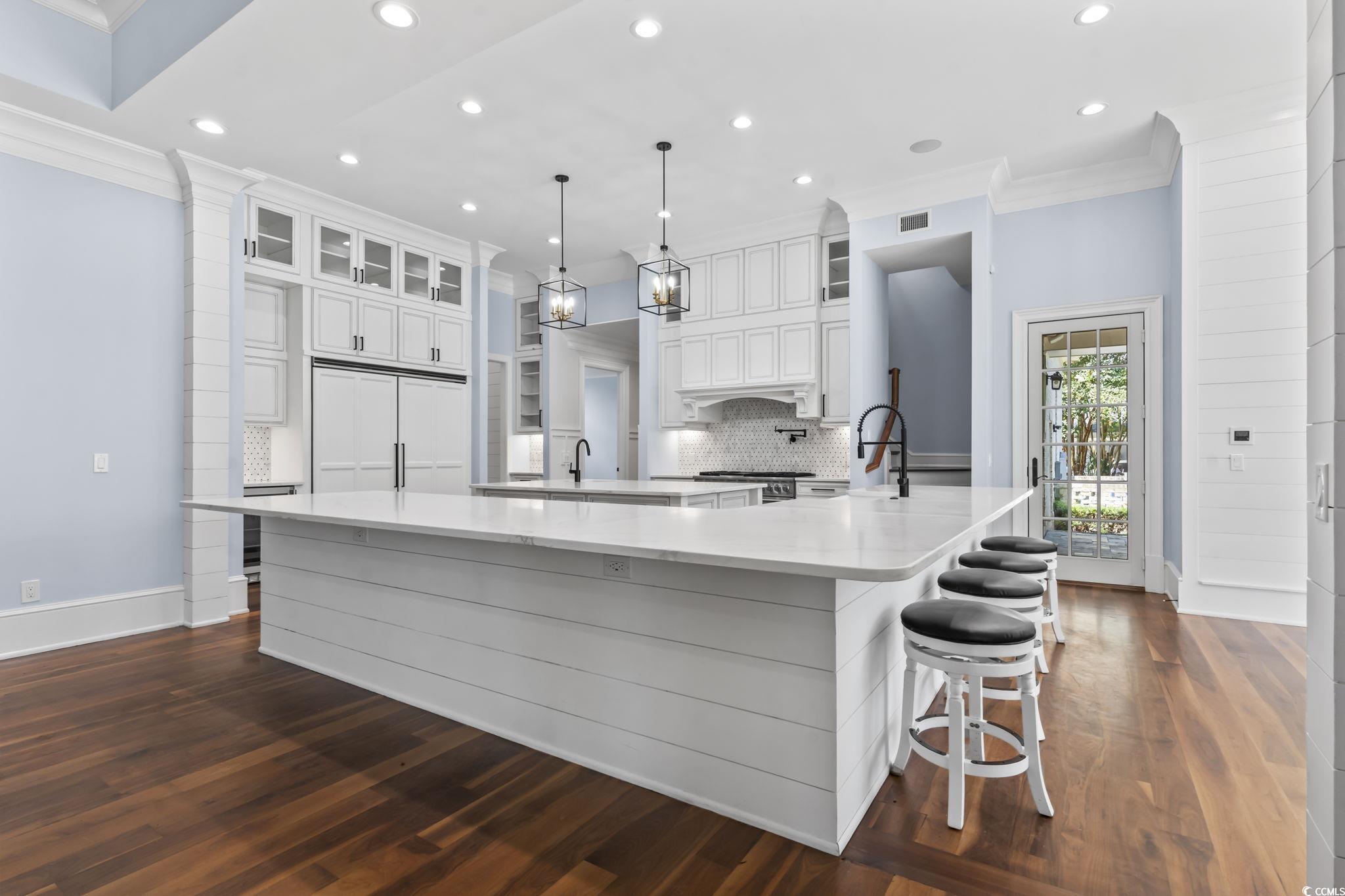 9318 Cove Drive Myrtle Beach, SC 29572 - Photo 16 of 40 Kitchen with white cabinetry, crown molding, hanging light fixtures, a breakfast bar, and light stone countertops