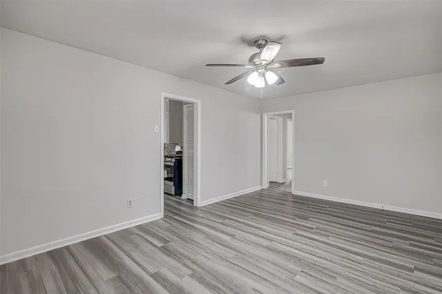 a view of an empty room with wooden floor and a ceiling fan