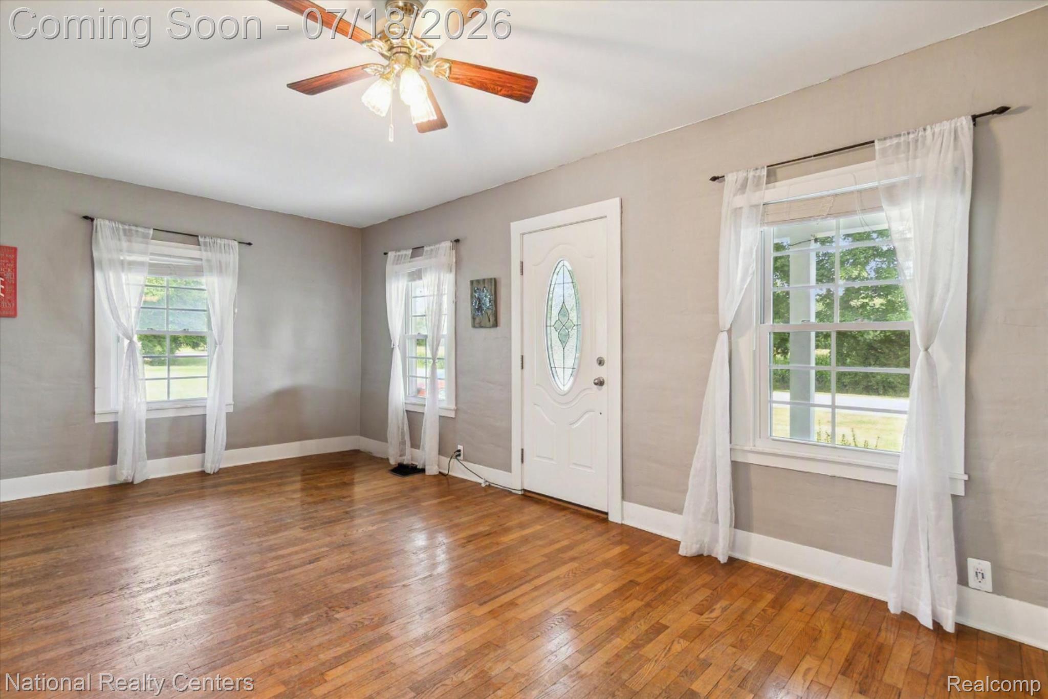 9589 Clinton Macon Road Tecumseh, MI 49286 - Photo 7 of 48 Interior room featuring wood-finish flooring, a white paneled entry door with an oval decorative glass insert, and a ceiling fan with light fixture