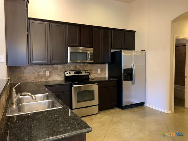 a kitchen with granite countertop a stove a microwave a refrigerator and cabinets