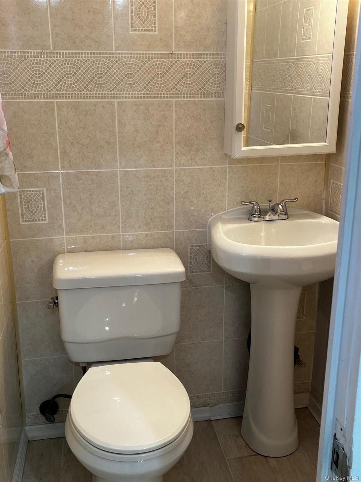 440 Mile Square Road Yonkers, NY 10701 - Photo 11 of 29 Bathroom featuring floor-to-ceiling ceramic tile, a decorative tile border, pedestal sink with chrome faucet, toilet, and a medicine cabinet with integrated mirror