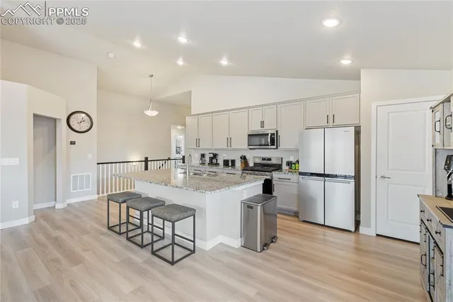 a kitchen with stainless steel appliances granite countertop a refrigerator a stove a sink a dining table and chairs with wooden floor