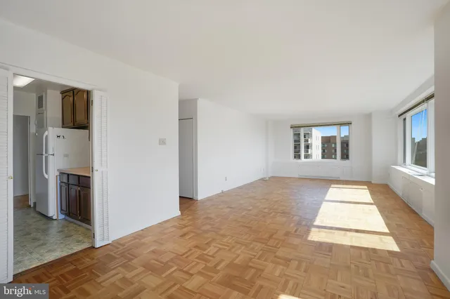 a view of an empty room with kitchen and window