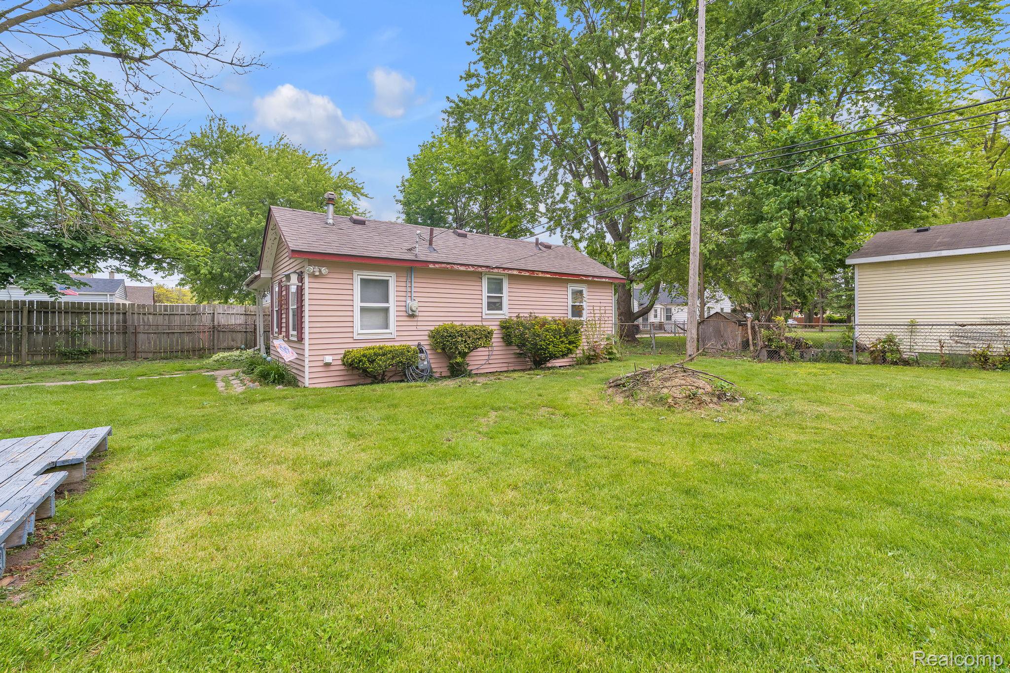 11063 Jackson Street Taylor, MI 48180 - Photo 24 of 27 Expansive green lawn surrounds the property, featuring a single-story residence with pink siding and a brown shingle roof