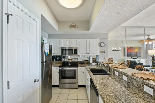 a large white kitchen with stainless steel appliances granite countertop a stove a sink dishwasher a refrigerator a oven with white cabinets and wooden floor