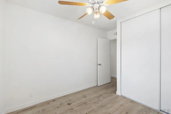 an empty room with a chandelier fan and wooden floor