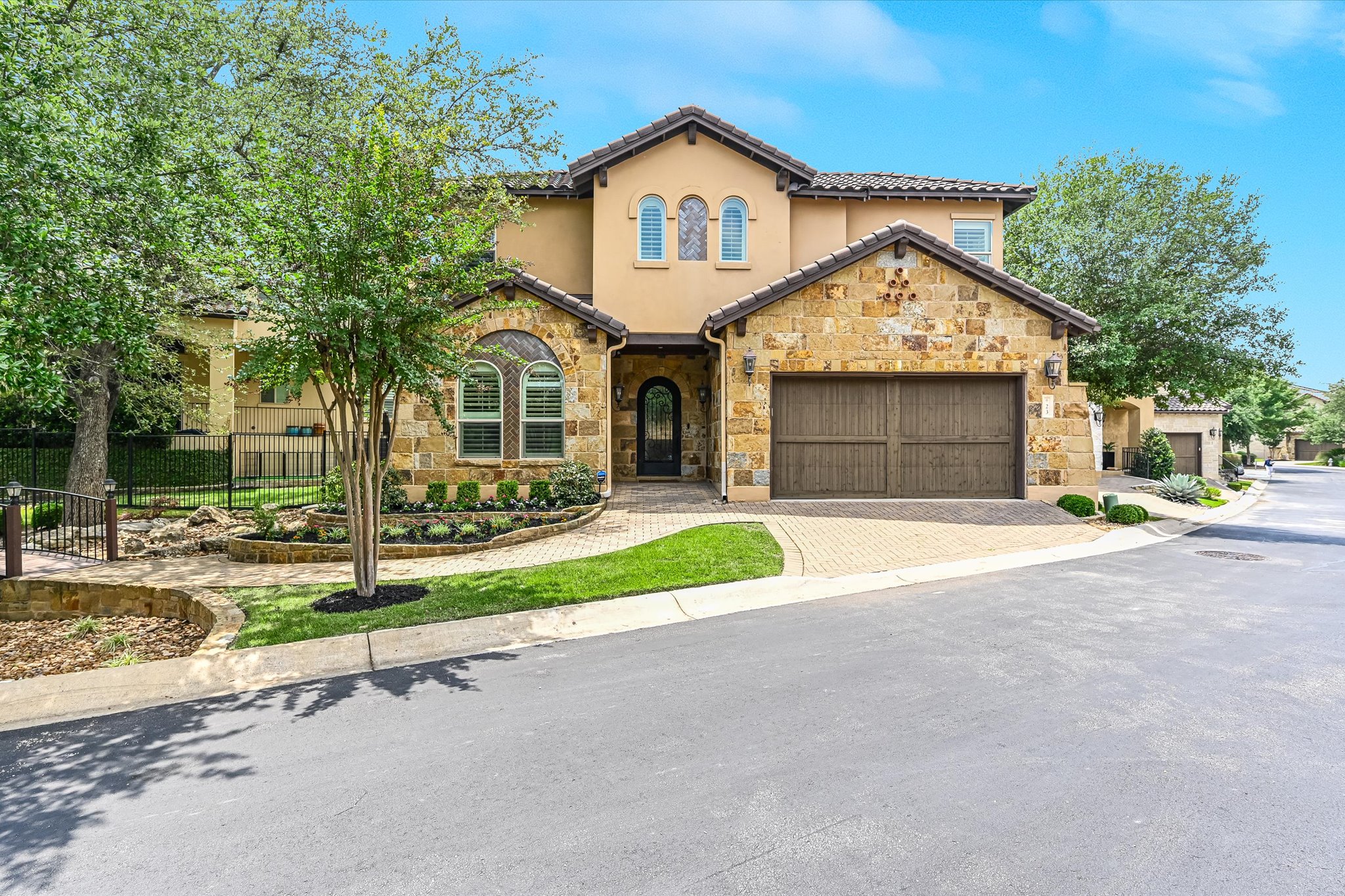 Stucco and stone facade property featuring an arched entry, decorative garage doors, and mature landscaping