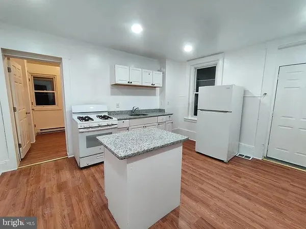a kitchen with granite countertop a sink stove a refrigerator and white cabinets with wooden floor