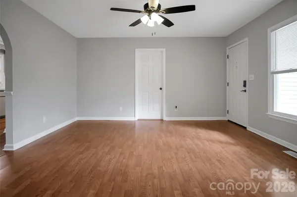 an empty room with wooden floor fan and windows