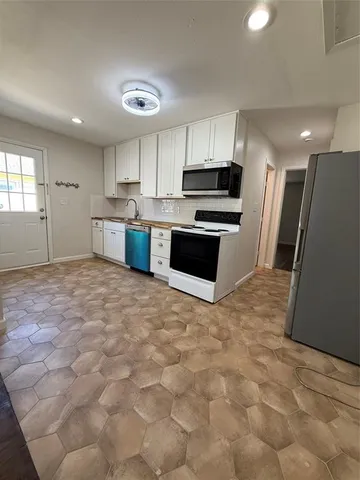 a large white kitchen with stainless steel appliances granite countertop a stove a sink a microwave and a refrigerator