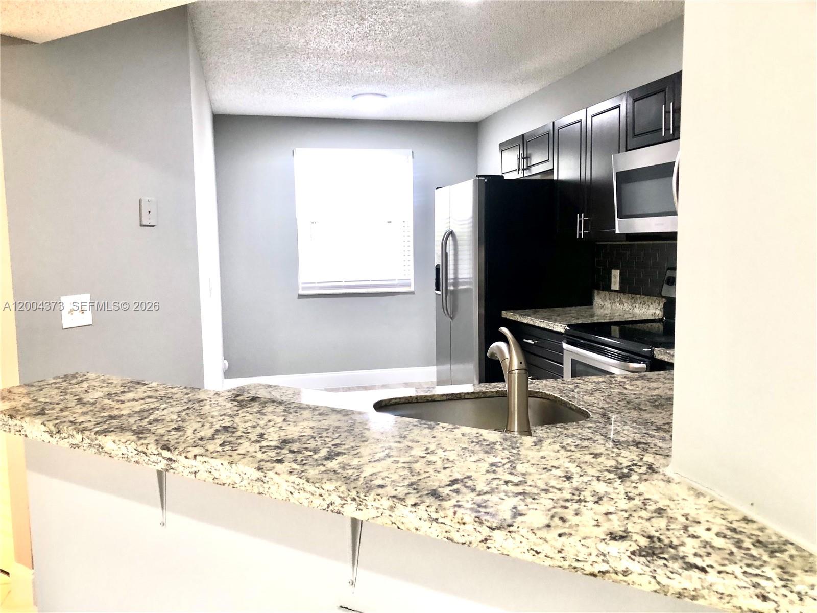 8761 Wiles Road, Unit 306 Coral Springs, FL 33067 - Photo 14 of 19 a kitchen with granite countertop a refrigerator and a sink
