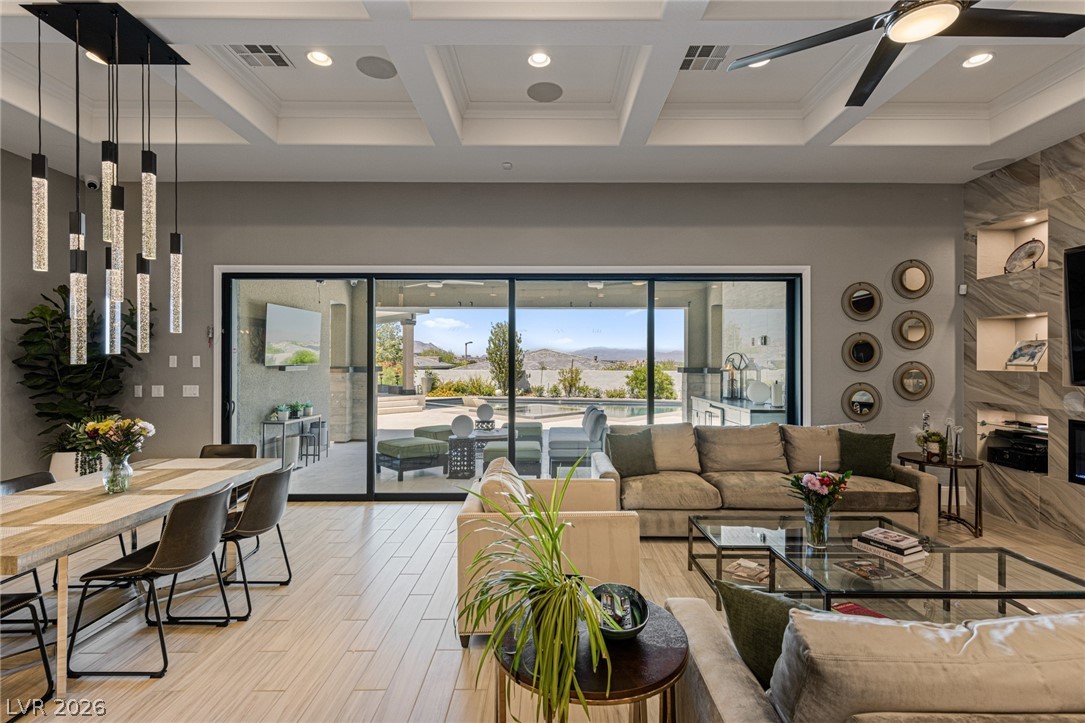 10118 Copper Edge Road Las Vegas, NV 89148 - Photo 7 of 48 An inviting open-concept living space features coffered ceilings, modern lighting, and a panoramic sliding glass door revealing mountain vistas.