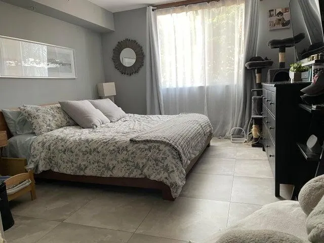 a bedroom with a bed a mirror on dresser and a flat tv screen on the dresser