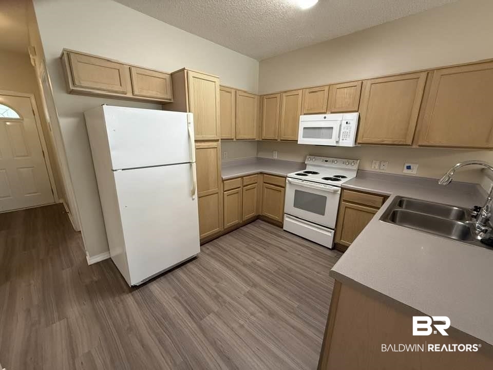 2651 South Juniper Street, Unit 401 Foley, AL 36535 - Photo 15 of 27 Kitchen featuring a sink, light brown cabinetry, white appliances, a textured ceiling, and wood finished floors