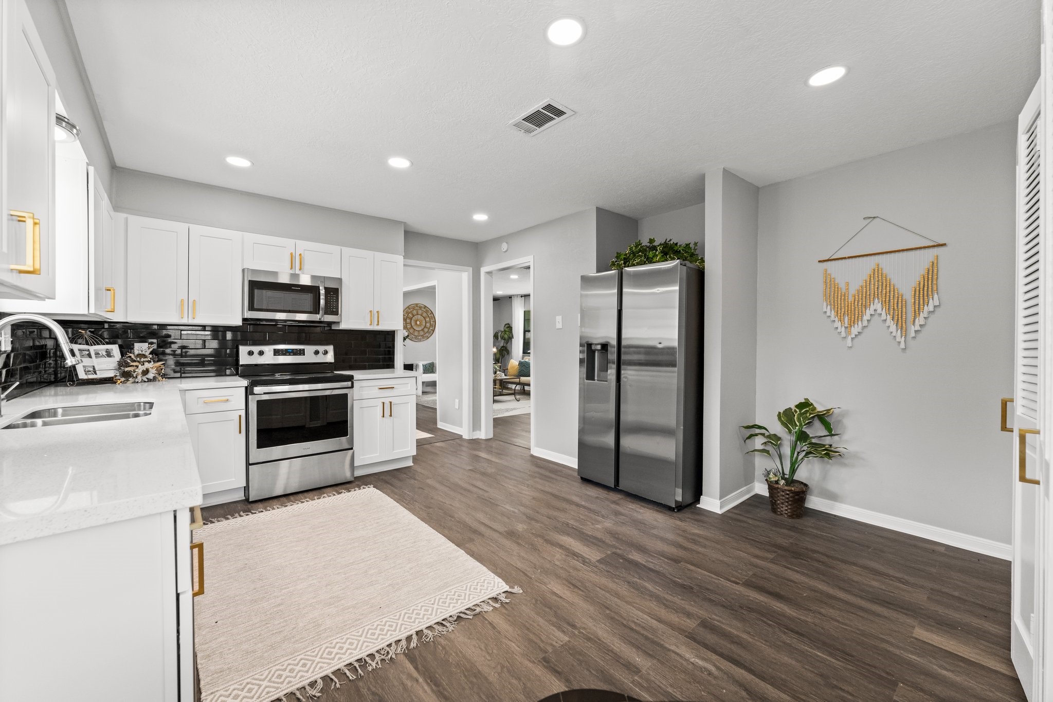 7280 Click Drive Beaumont, TX 77708 - Photo 11 of 39 Modern kitchen with sleek stainless steel appliances, white cabinetry, and a black tile backsplash. The space features wood-look flooring, recessed lighting, and tasteful decor, offering a clean and inviting atmosphere.