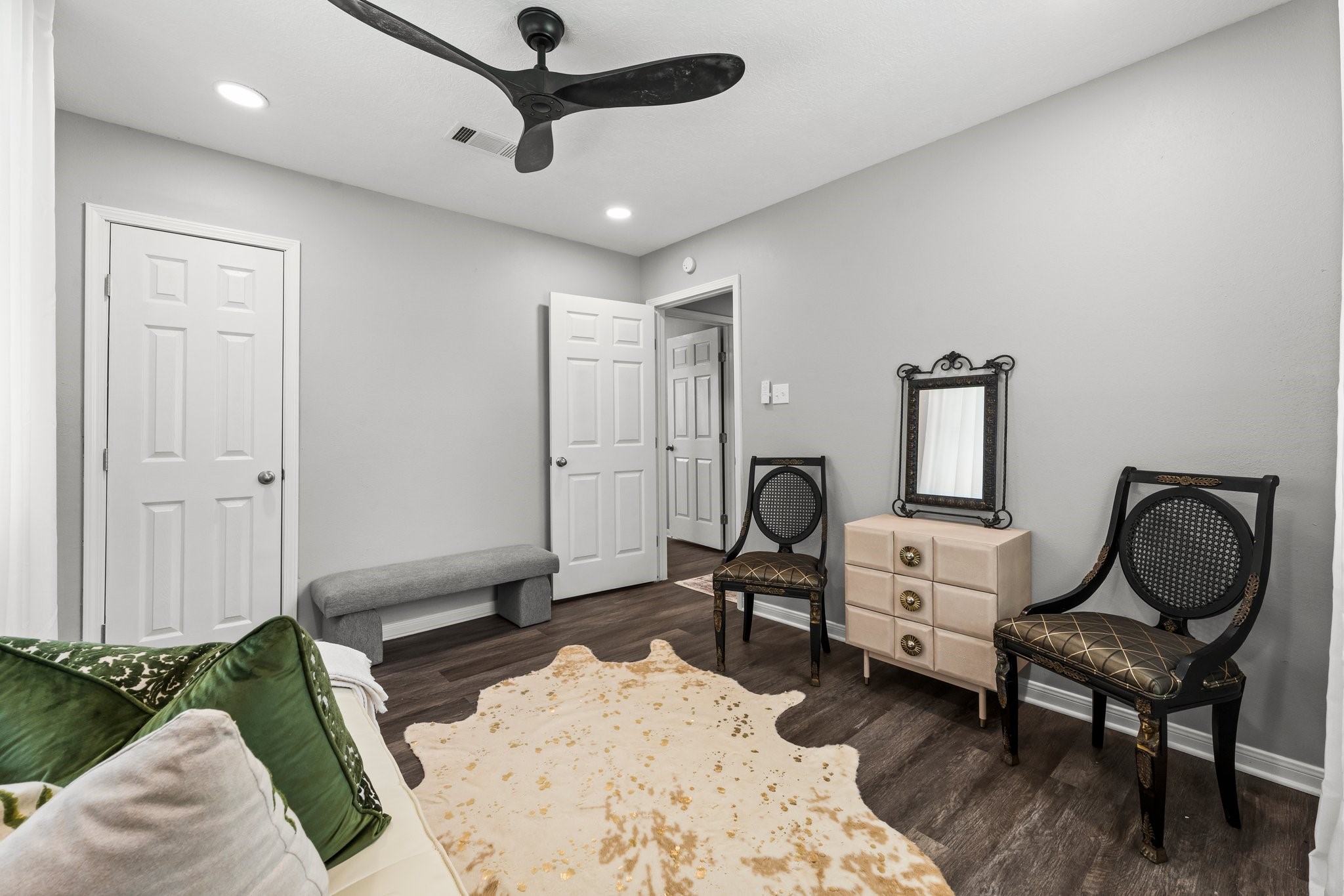 7280 Click Drive Beaumont, TX 77708 - Photo 21 of 39 This room features a sleek, modern design with gray walls and dark wood flooring. It includes a ceiling fan, two decorative chairs, a small dresser with a mirror, and a cozy bench. The space is well-lit with recessed lighting and has a stylish, minimalist vibe.