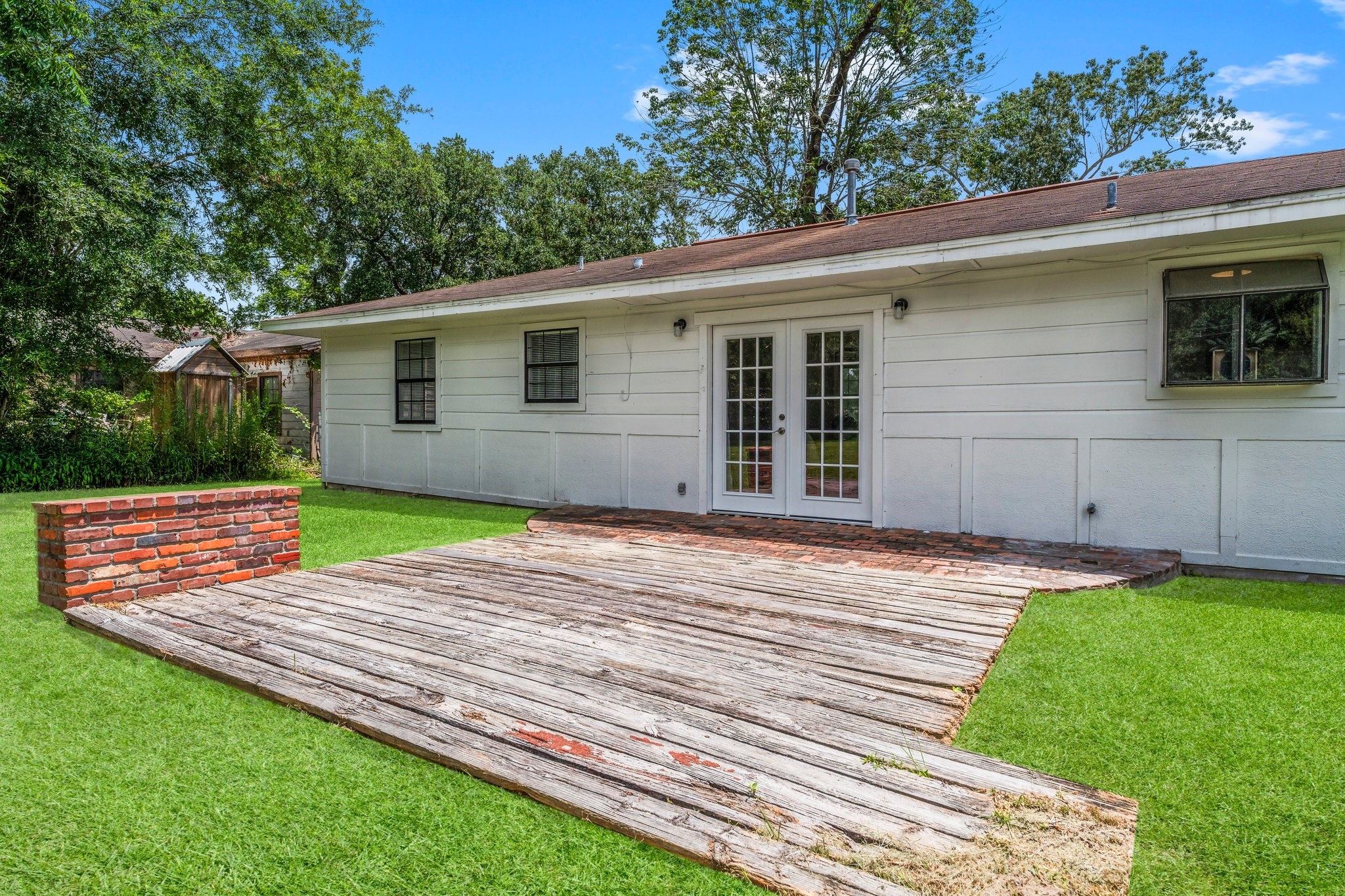 7280 Click Drive Beaumont, TX 77708 - Photo 27 of 39 This photo showcases a backyard with a spacious wooden deck, bordered by a small brick wall. It features a well-maintained lawn and a white exterior of a house with French doors, offering a great space for outdoor activities and relaxation.