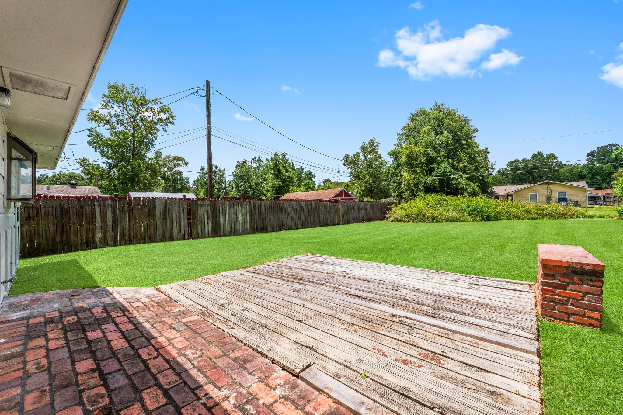 7280 Click Drive Beaumont, TX 77708 - Photo 28 of 39 Spacious backyard with a mix of brick and wood patio, lush green lawn, and a wooden privacy fence, perfect for outdoor activities and relaxation.