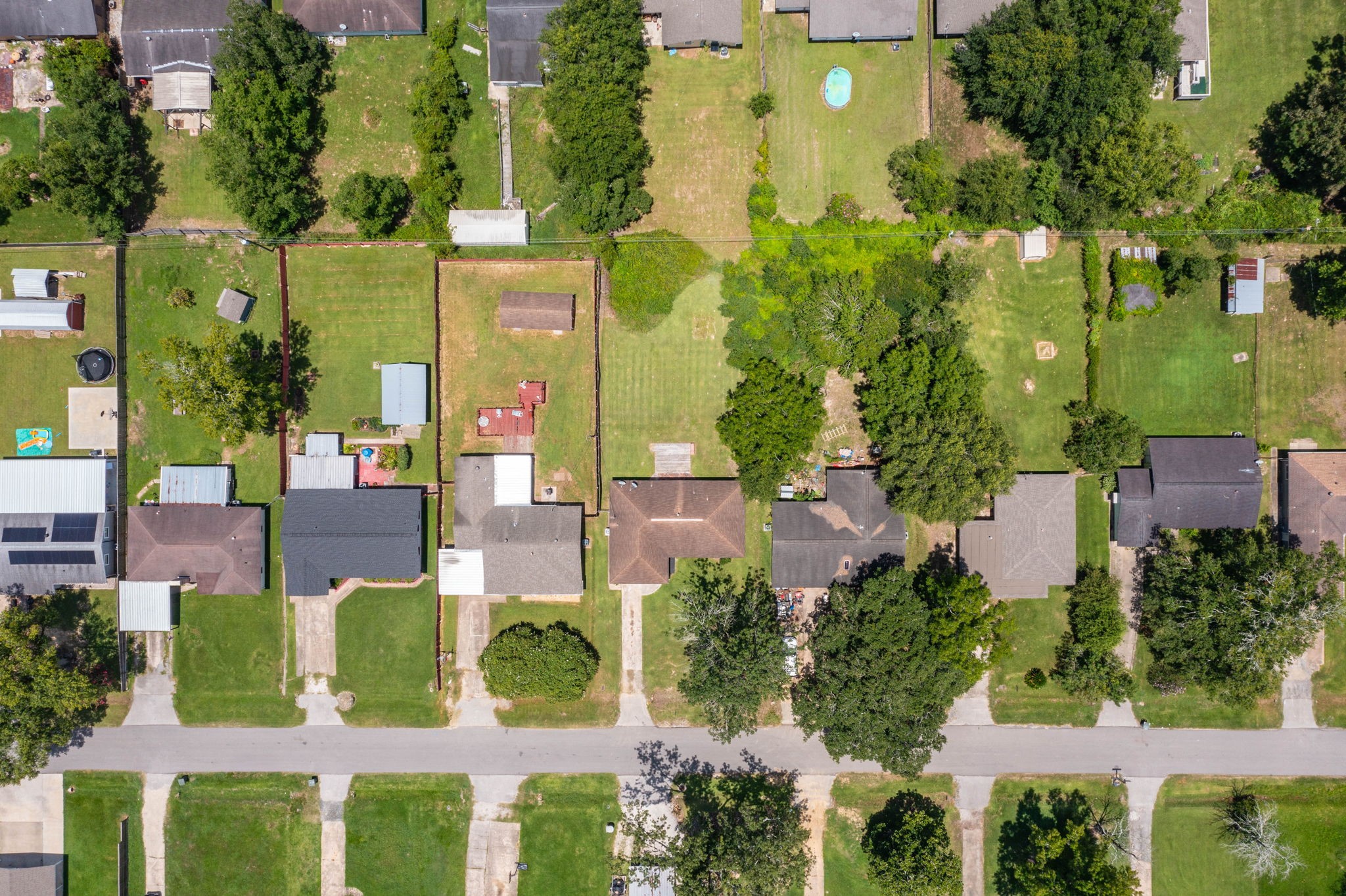 7280 Click Drive Beaumont, TX 77708 - Photo 37 of 39 This aerial view showcases a suburban neighborhood with neatly arranged single-family homes. Each property features well-maintained lawns and backyards, some with trees and small structures. The street layout is straightforward, and the area appears peaceful and green, indicating a family-friendly environment.