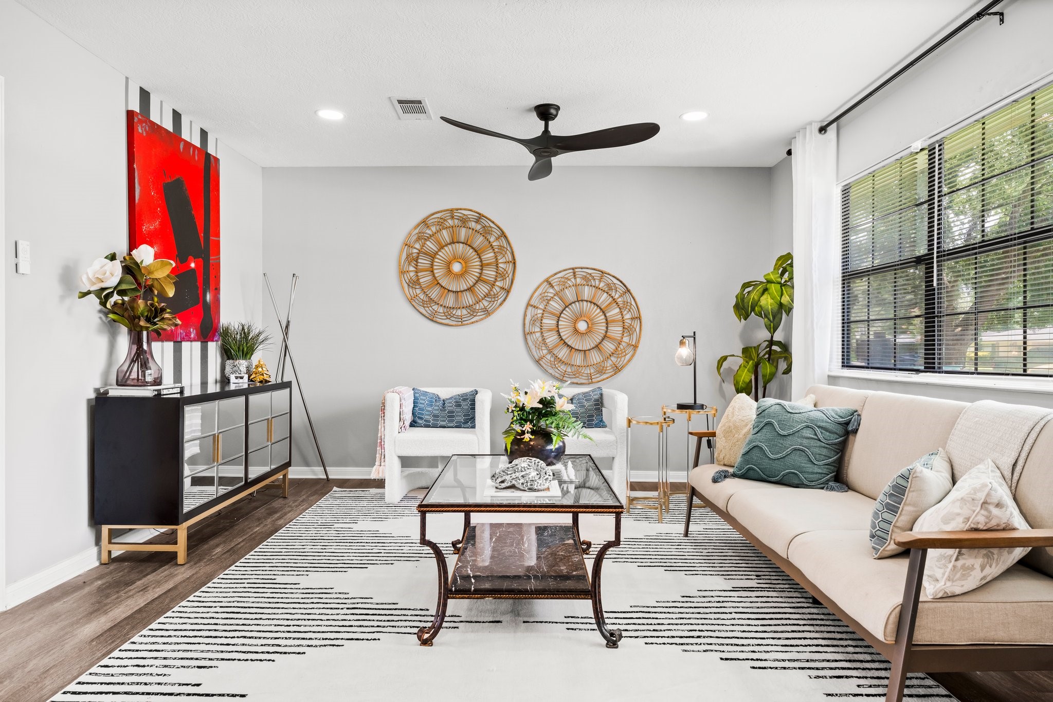 7280 Click Drive Beaumont, TX 77708 - Photo 7 of 39 This living room features a modern and cozy design with a neutral color palette. It includes a large window for natural light, stylish decor, a comfortable sofa, and a ceiling fan. The space is accented with a patterned rug and contemporary artwork, creating a welcoming atmosphere.