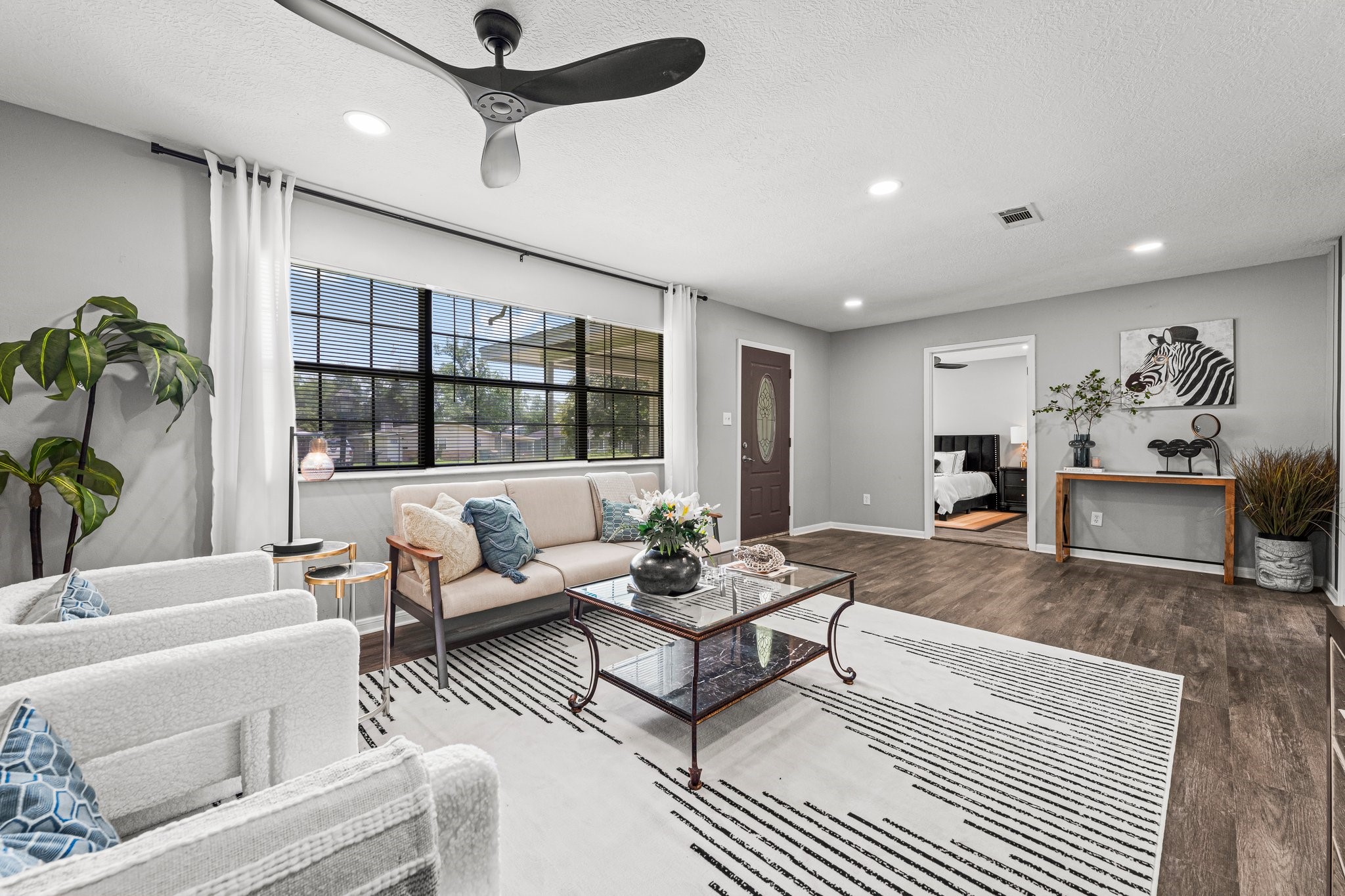 7280 Click Drive Beaumont, TX 77708 - Photo 8 of 39 This living room features a modern design with neutral tones, hardwood floors, and abundant natural light. It includes stylish furniture, a ceiling fan, and a large window, creating a welcoming and airy atmosphere.