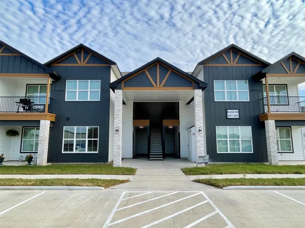 a view of a brick house with a yard plants and large trees