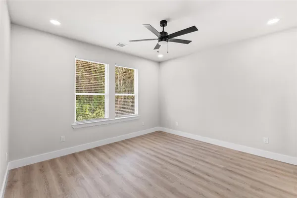 an empty room with wooden floor fan and windows