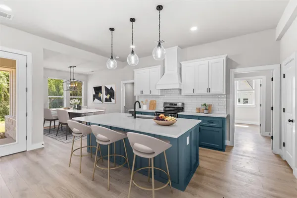 a kitchen with stainless steel appliances granite countertop a stove a refrigerator a kitchen island a sink and white cabinets with wooden floor