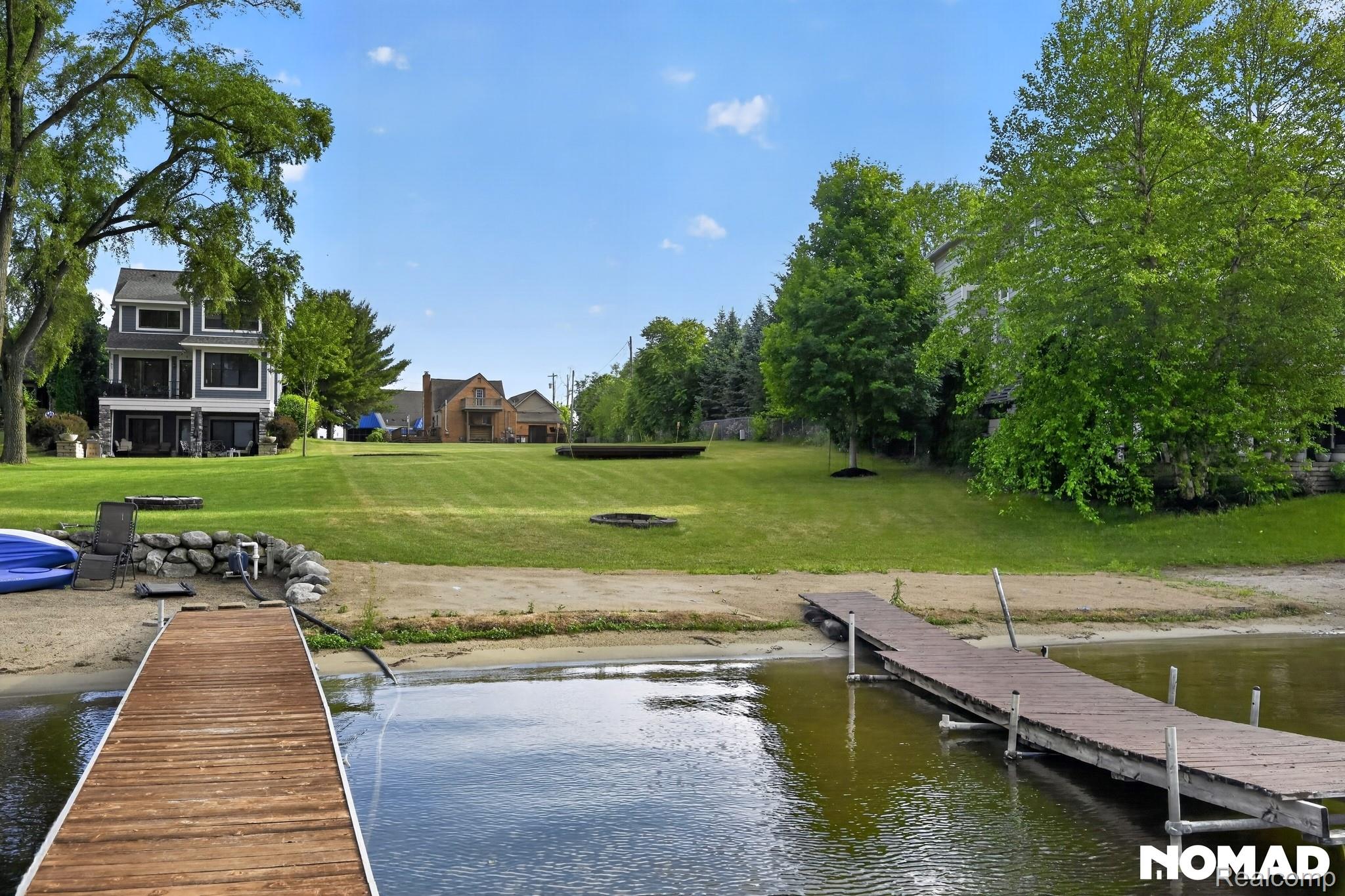 8315 Hilton Road Brighton, MI 48114 - Photo 24 of 26 Waterfront property featuring two wooden docks, a sandy beach area, and a tiered grassy lawn