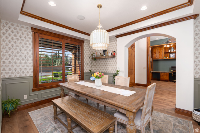 687 South 2080th Street East Springville, UT 84663 - Photo 10 of 149 Dining space featuring wood-finish flooring, a large window with wood shutters, decorative ceiling trim, and an arched entryway to an additional room with built-in cabinetry
