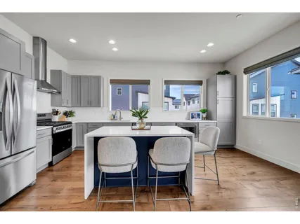a kitchen with stainless steel appliances kitchen island granite countertop a dining table chairs and a refrigerator