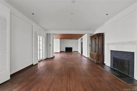 a view of an empty room with wooden floor a fireplace and a window