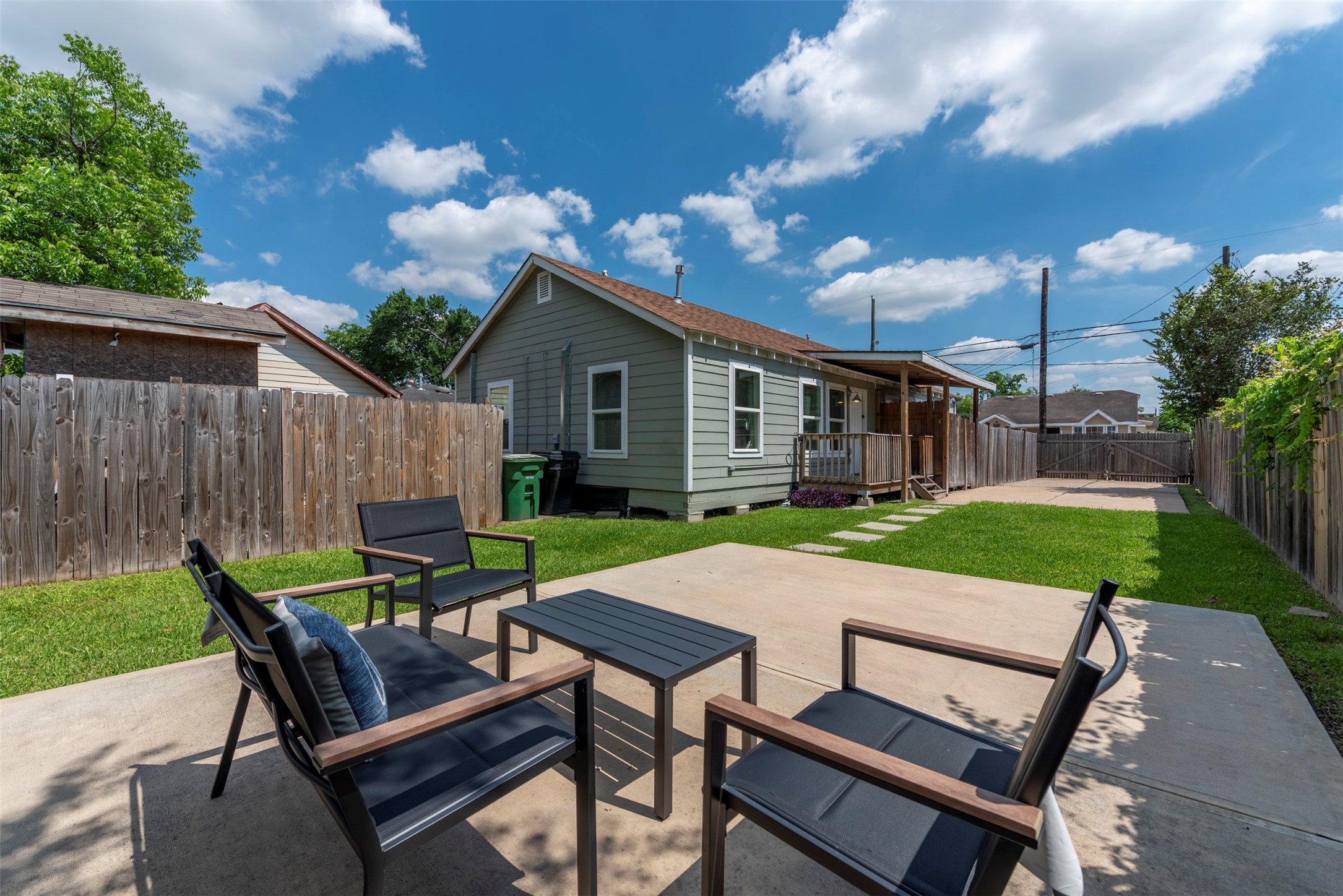 1121 Panama Street Houston, TX 77009 - Photo 29 of 35 Backyard entertaining area with poured concrete patio, modern outdoor seating, manicured lawn, concrete stepping stone path, and covered back porch with wood beam detailing.