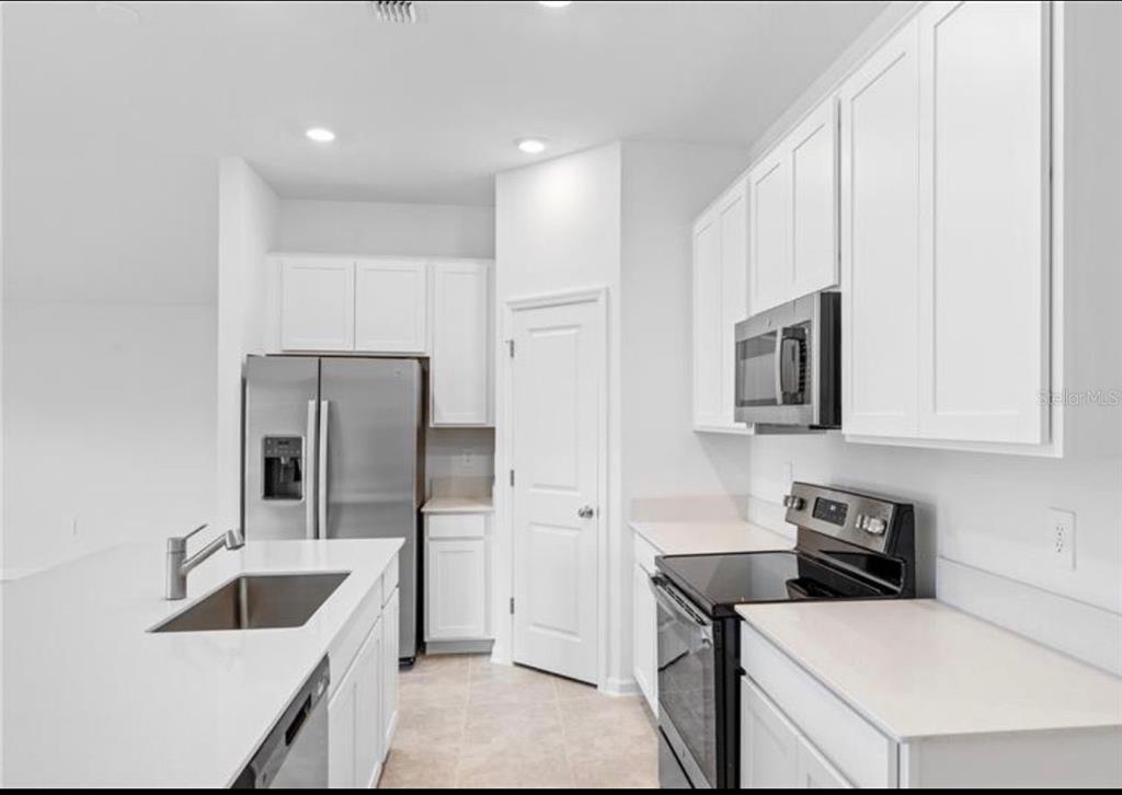 352 Heroic Road Davenport, FL 33837 - Photo 4 of 19 a kitchen with white cabinets and stainless steel appliances