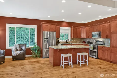 a kitchen with stainless steel appliances granite countertop a stove top oven a sink dishwasher a dining table and chairs with wooden floor