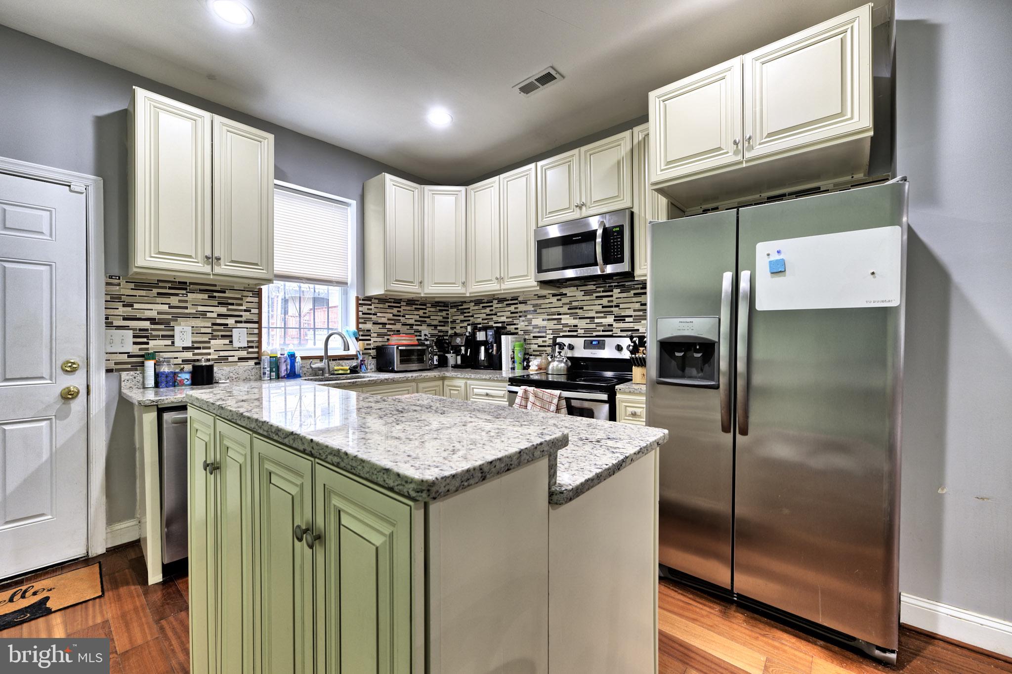 318 East 28th Street Baltimore, MD 21218 - Photo 8 of 20 a kitchen with stainless steel appliances granite countertop a refrigerator a stove a sink and white cabinets with wooden floor