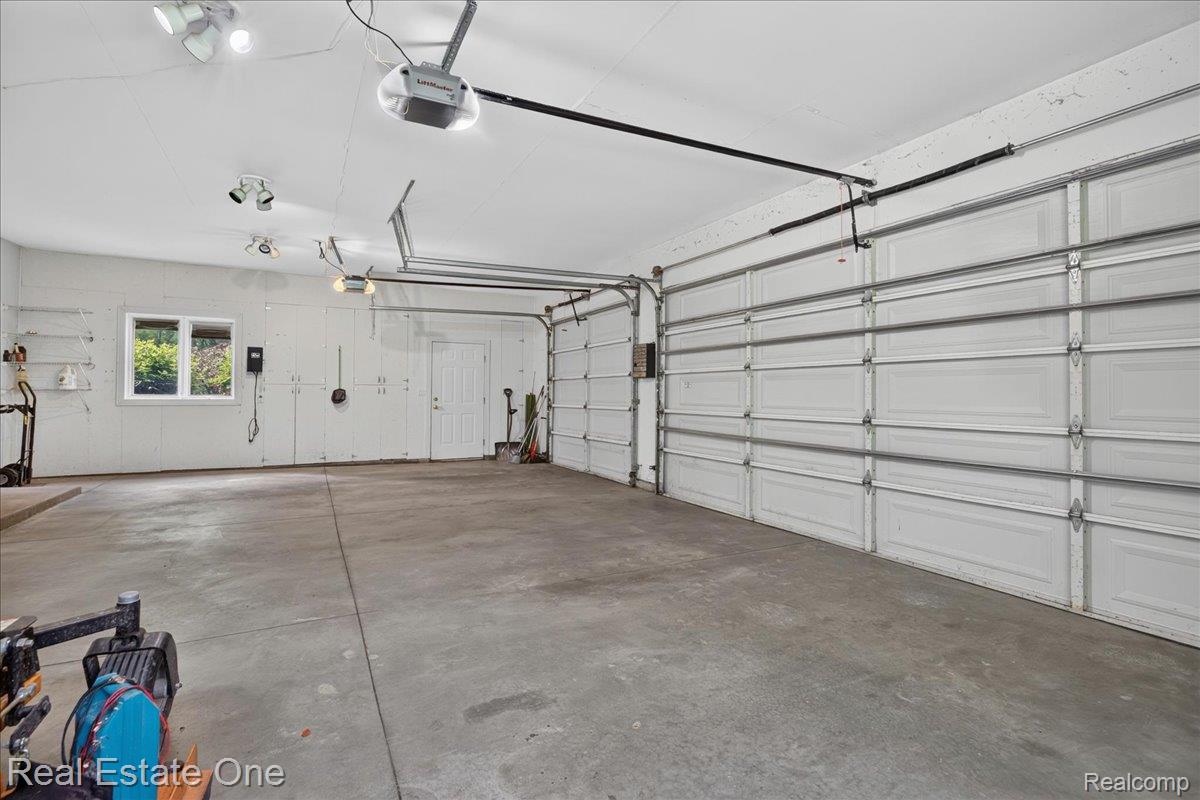 425 Courtney Road Leonard, MI 48367 - Photo 34 of 89 Spacious garage featuring a concrete floor, two white paneled garage doors, overhead lighting, a white pedestrian door, and a horizontal window