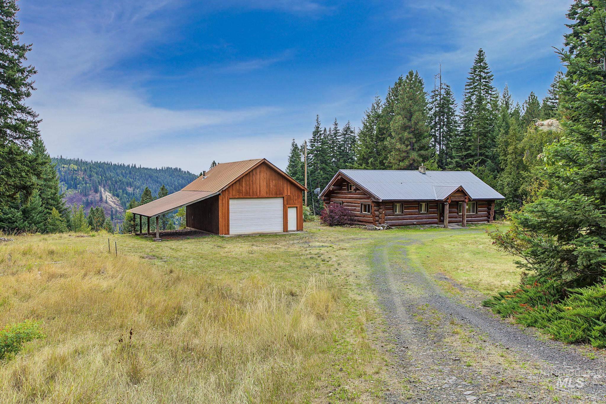 2926 Wells Bench Road Orofino, ID 83544 - Photo 42 of 48 Log cabin with covered entry and metal roof, accompanied by a detached barn featuring a covered lean-to and roll-up garage door