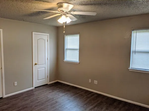 an empty room with wooden floor chandelier fan and windows